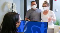 A patient and her partner, wearing masks, check in at the front desk of a medical office