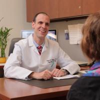 Male physician at desk smiles at patient.